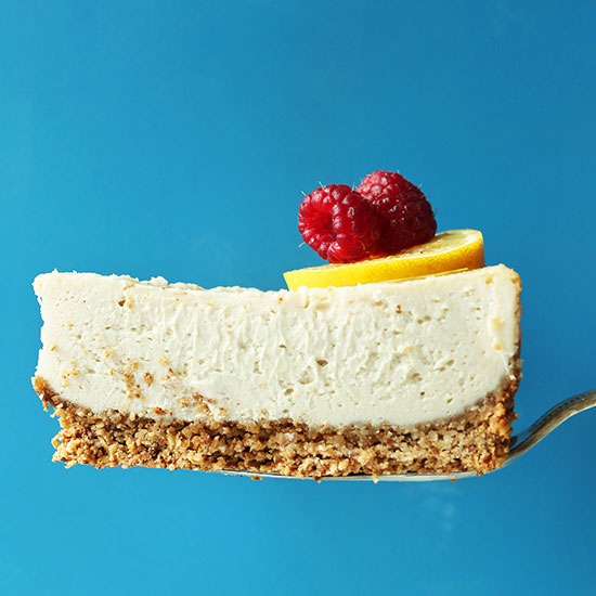 Holding up a slice of Easy Baked Vegan Cheesecake topped with lemon and raspberries